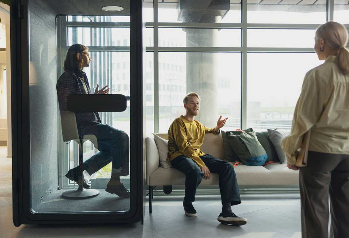 A man in a meeting in a phone booth, two other people talking outside