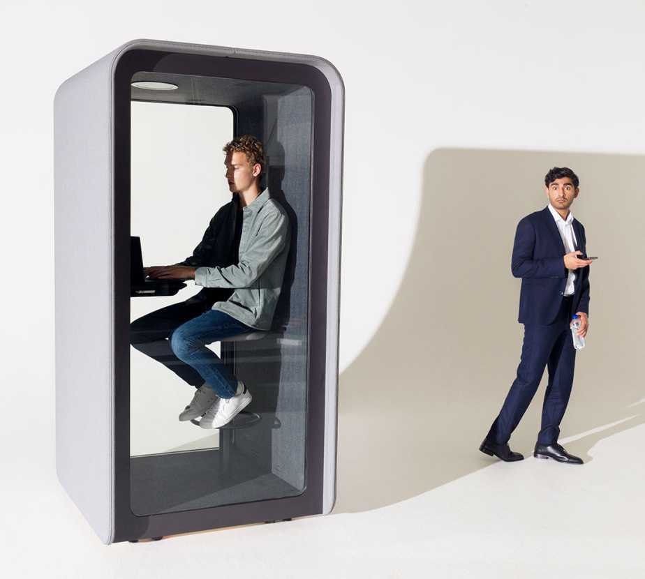 A man working in a phone booth and the other is standing outside